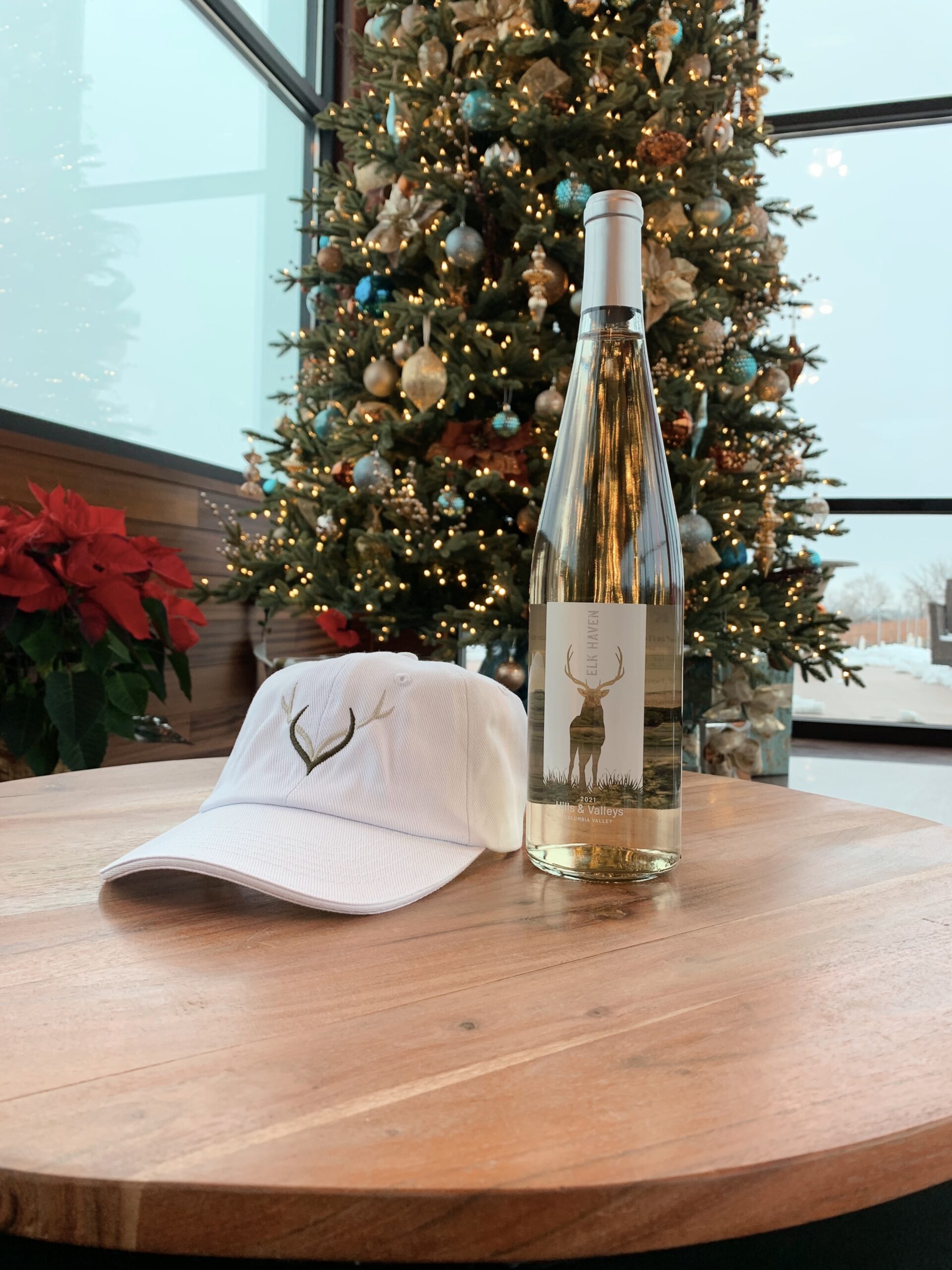 white baseball cap with elk haven logo sitting next to wine bottle